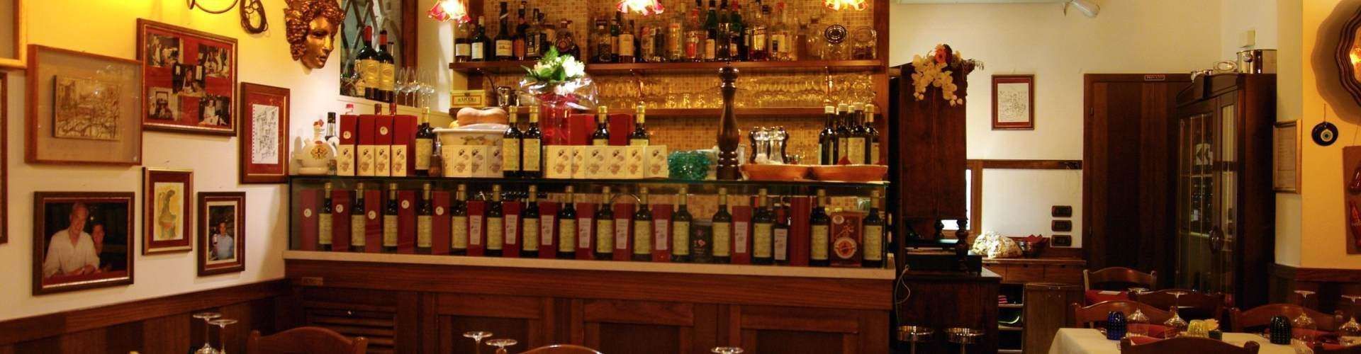 Interior view of a cozy, wood-paneled restaurant bar with numerous wine bottles lined on the shelves and framed pictures.