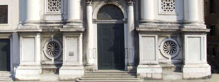 The stone facade of a classical building features a central dark doorway, columns, and ornate circular stone carvings.