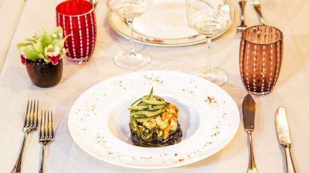 A plated seafood and vegetable dish sits on a table set with wine glasses, colorful tumblers, and silverware.