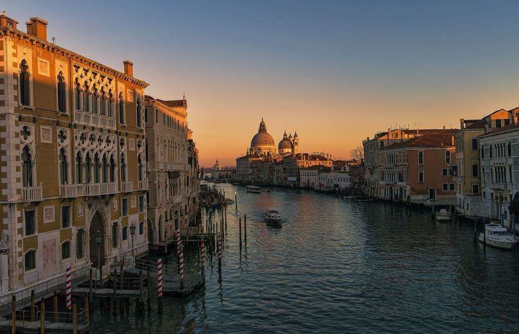 Venice's Grand Canal at sunset, with historic ornate buildings lining the water and the Santa Maria della Salute in view.
