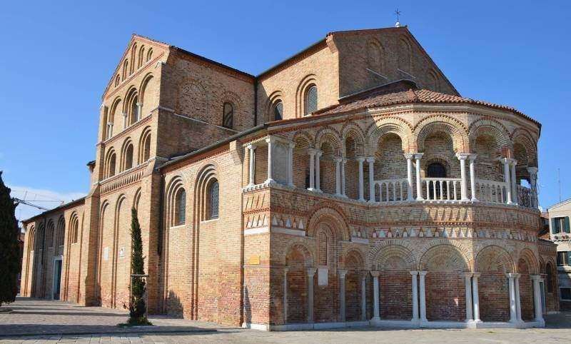 Brick exterior of the Byzantine-style Church of Santa Maria e San Donato on Murano island under a clear blue sky.