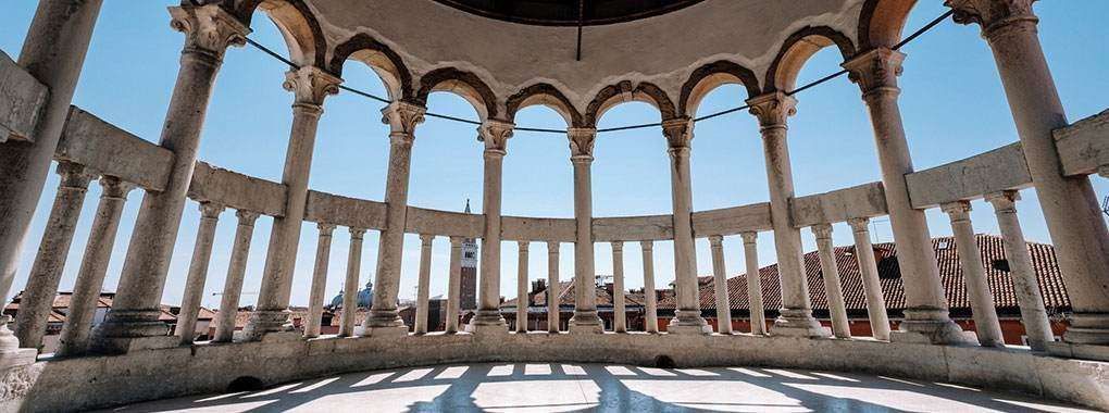 Curved stone colonnade with arches overlooking a city skyline under a clear blue sky.
