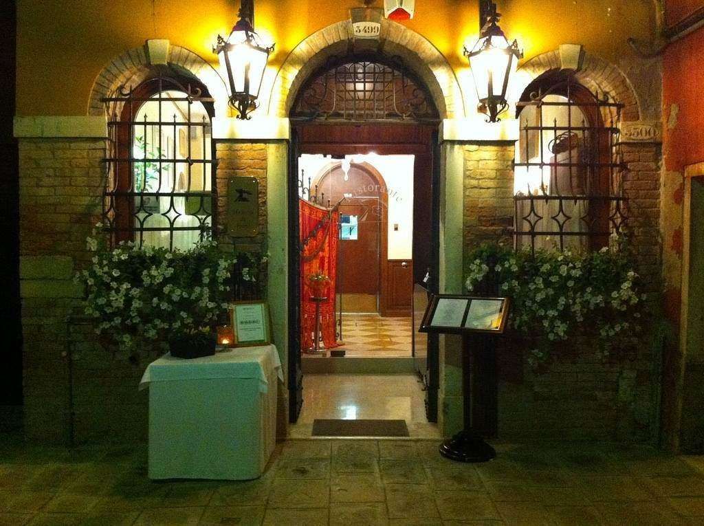 An arched entrance to a warmly lit restaurant at night, flanked by two wrought-iron lanterns and window grills.