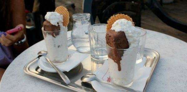 Two glasses of chocolate ice cream with whipped cream and wafer cookies served on a metal tray on a round table.