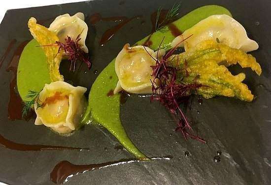 Plated meal featuring three tortellini, crispy fried zucchini blossoms, and green pea puree on a dark slate surface.