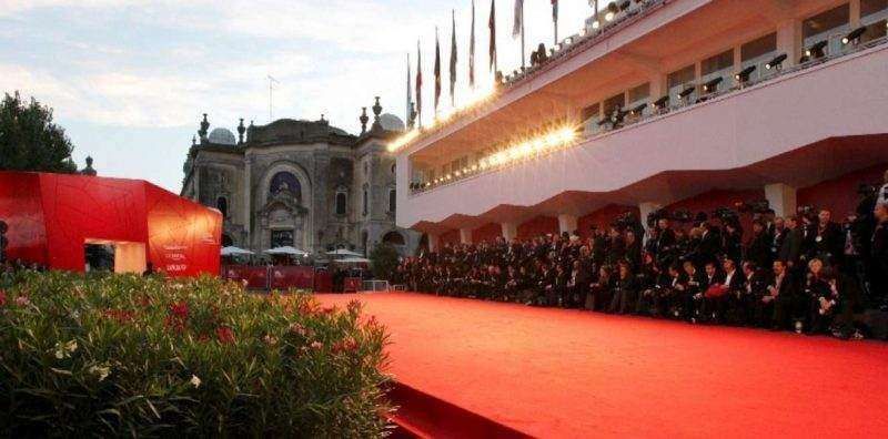A red carpet walkway lined with a crowd of people outside an ornate building at a film festival.