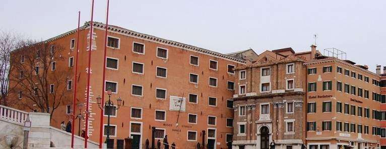 A low-angle view of two historic red brick buildings in Venice, Italy, separated by a narrow alley.