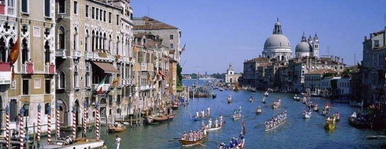 A wide view of Venice's Grand Canal with traditional rowboats and historical buildings under a clear blue sky.