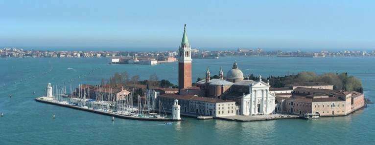 A high-angle view of San Giorgio Maggiore island in Venice, Italy, featuring a large church, campanile, and a marina.