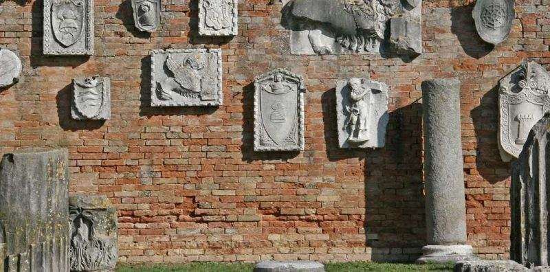 Stone coats of arms and reliefs displayed on an old brick wall in an outdoor archaeological site.