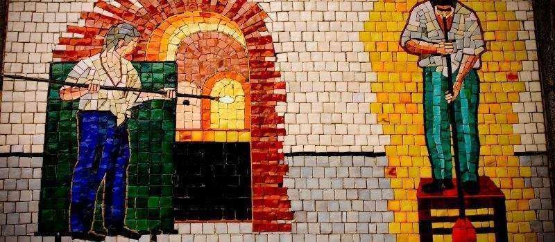 A mosaic showing two glassblowers at work, with one gathering molten glass from a furnace and the other shaping a piece.