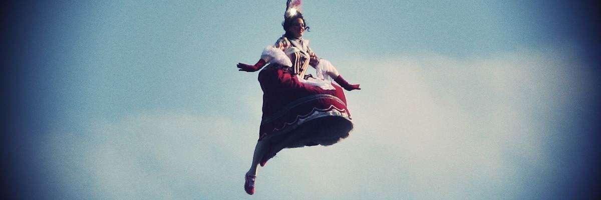A figure in a ornate red and white costume floats in a blue sky.