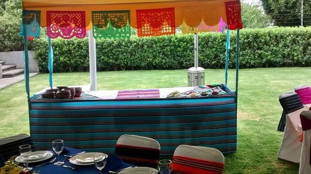 Una mesa preparada para una fiesta con platos, vasos, sillas y un dosel.