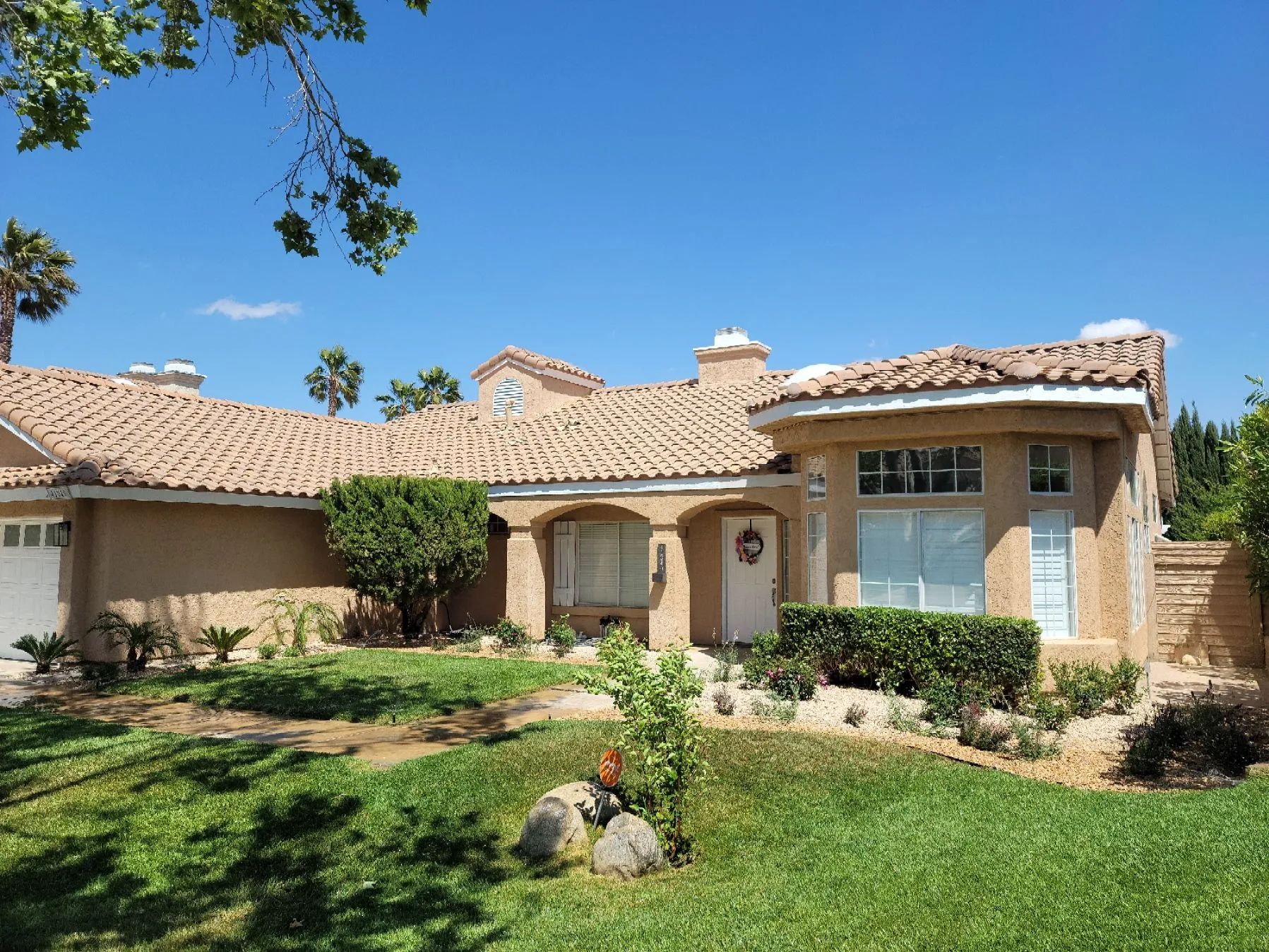 Tan stucco house with terracotta tile roof, blue sky, and green lawn.