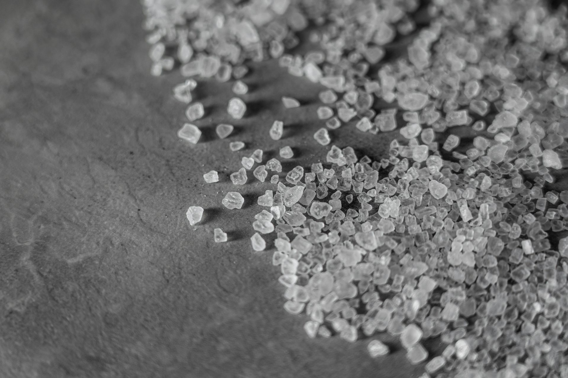 Scattered coarse salt crystals on a dark gray surface.