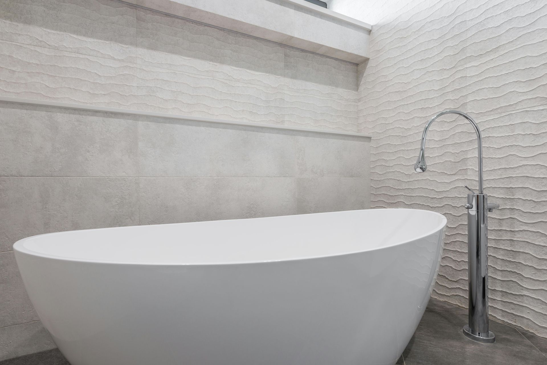 White freestanding bathtub with chrome faucet against textured wall in a modern bathroom.
