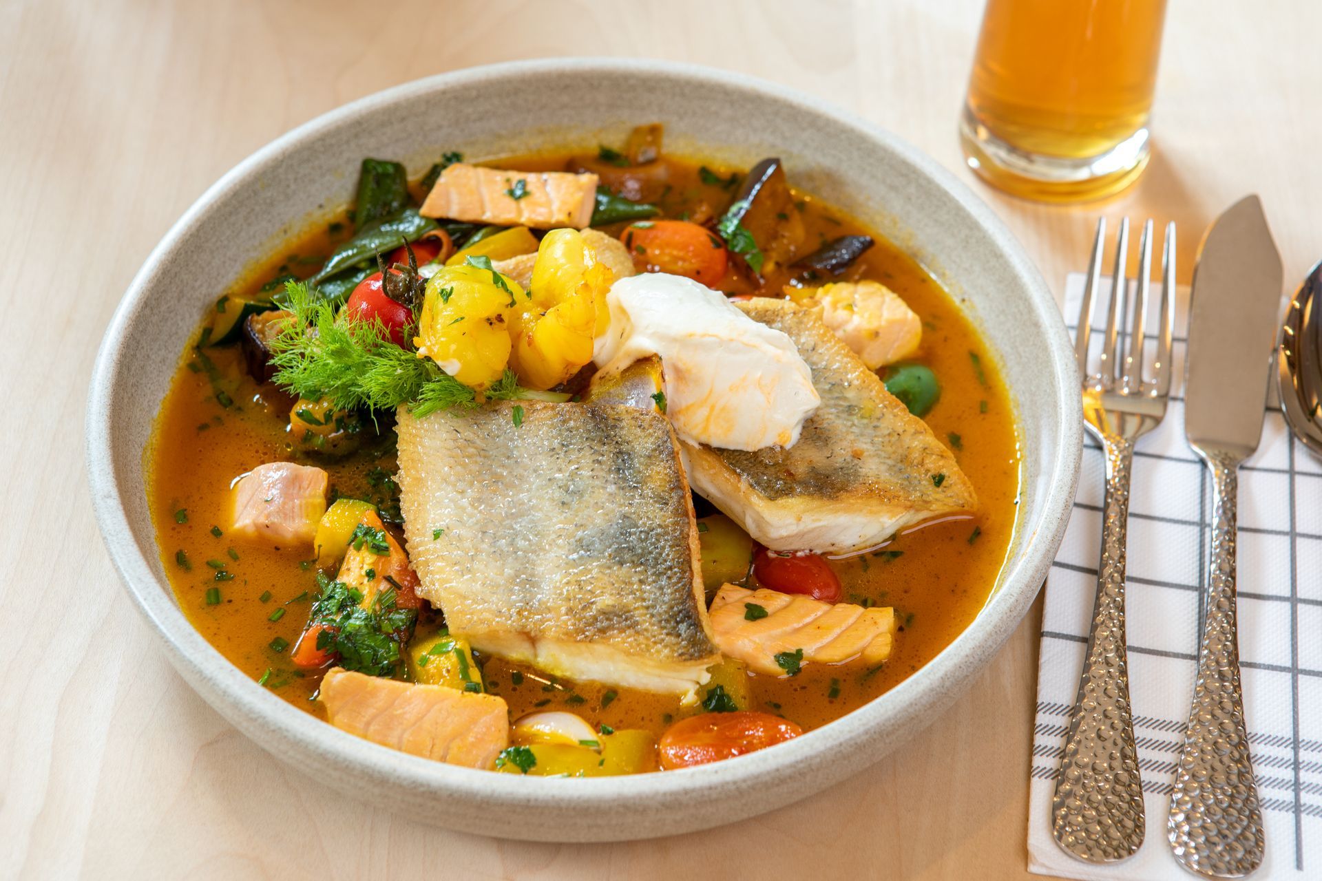 Schüssel mit Meeresfrüchteeintopf mit Fisch, Gemüse und Kräutern; serviert mit Besteck und Getränk.