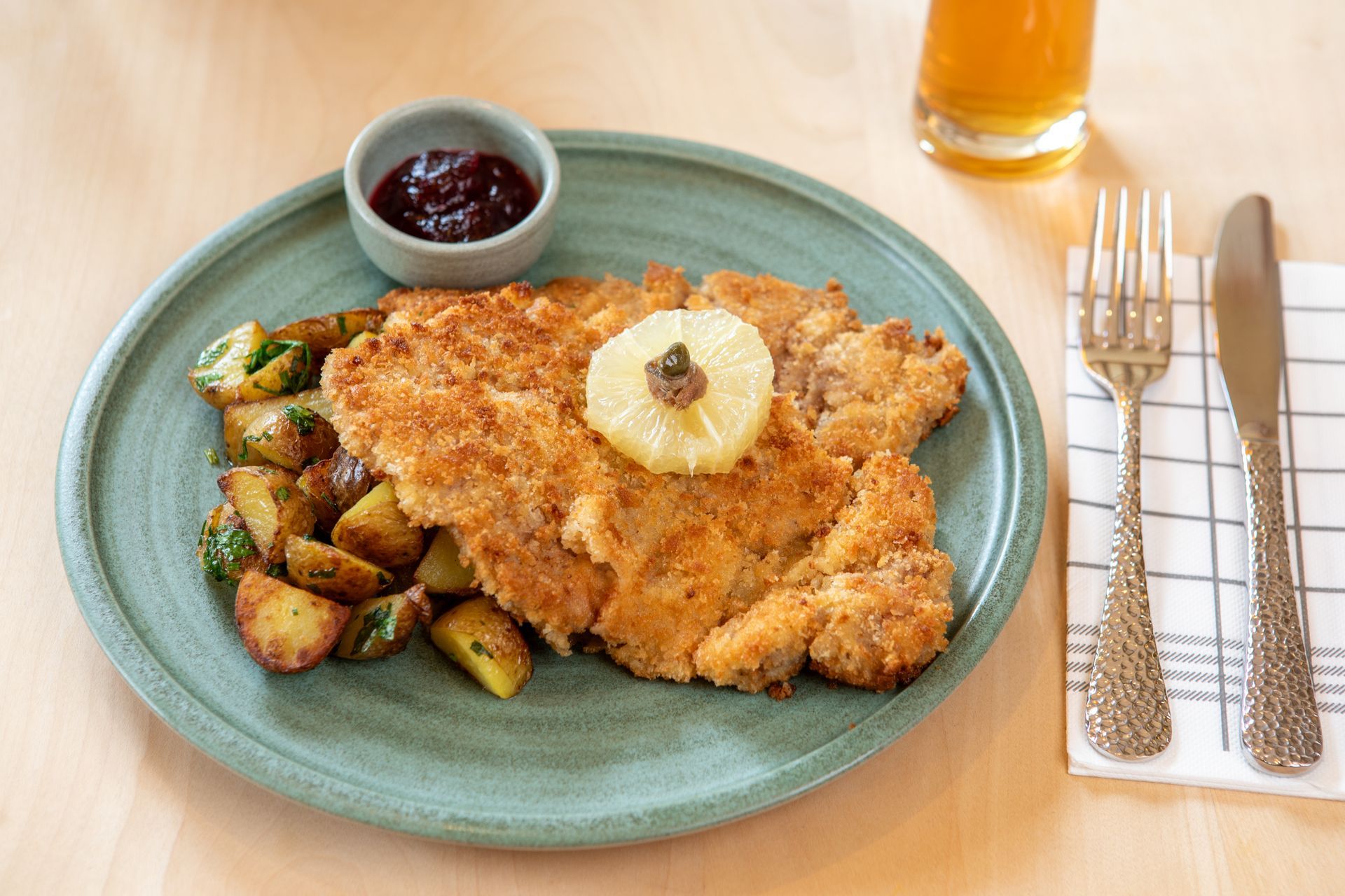 Paniertes Schweinekotelett mit Kartoffeln, Beeren und Ananas auf einem Teller mit Besteck.