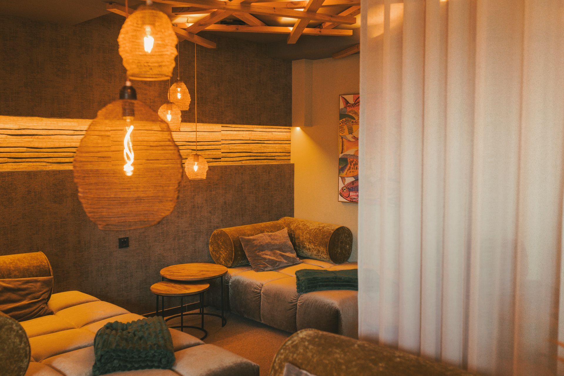 Gemütlicher Ruheraum mit hängenden Flechtlampen, Sitzgelegenheiten und transparenten Vorhängen. Warme, einladende Farbtöne.