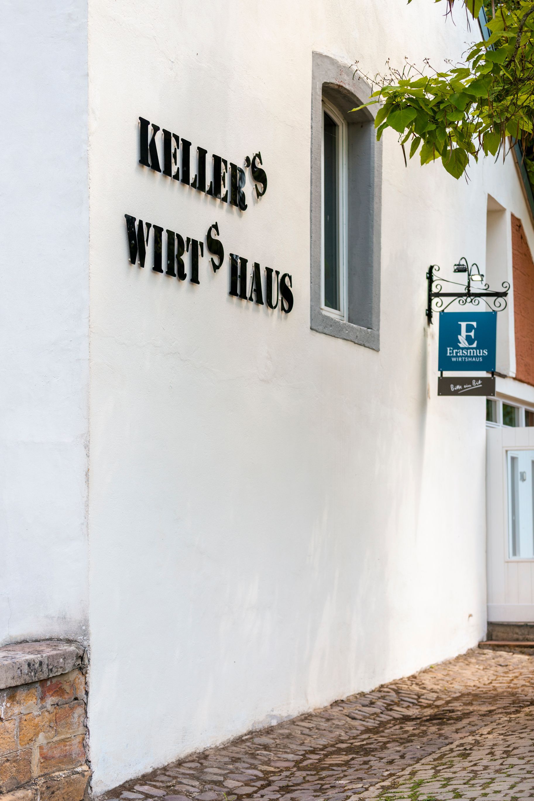 Ein weißes Gebäude mit einem Schild an der Seite, auf dem „Keller's Wirtshaus“ steht