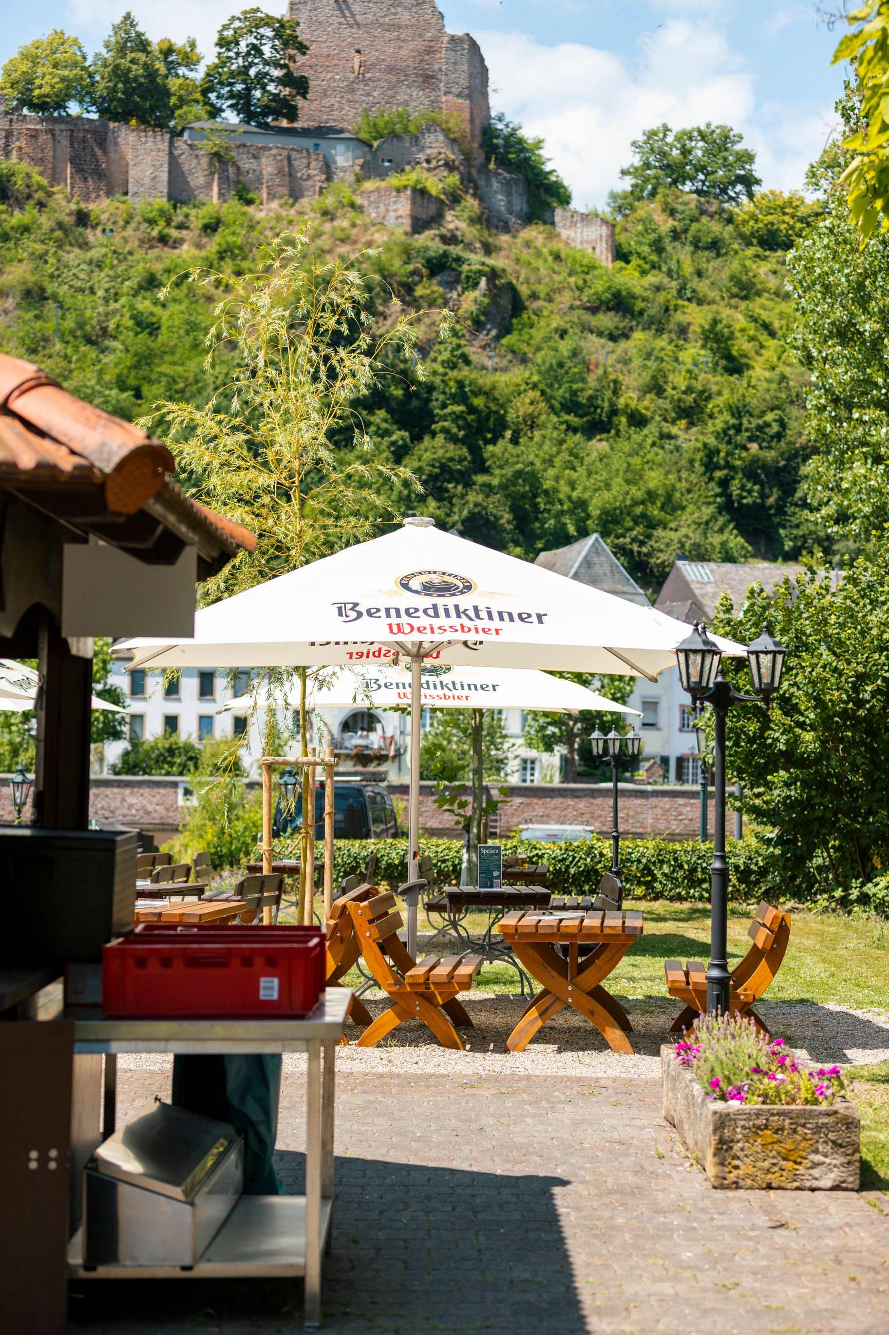 Sitzbereich im Freien mit Sonnenschirmen, Stühlen, Tisch und einer Steinburg auf einem Hügel.