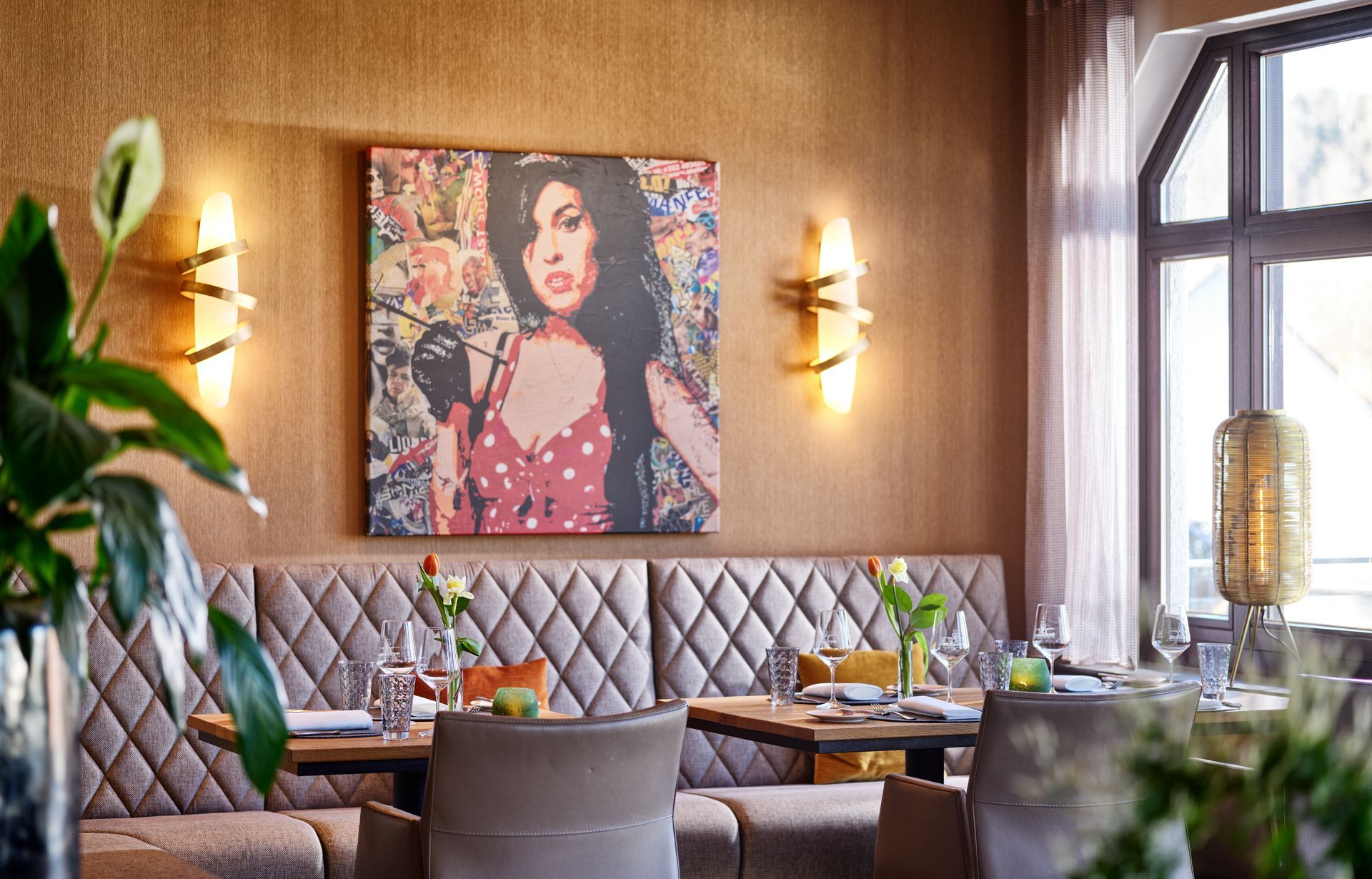 Essbereich des Restaurants mit Kunstwerken von Amy Winehouse, Sitzgelegenheiten, gedeckten Tischen und Wandleuchten.