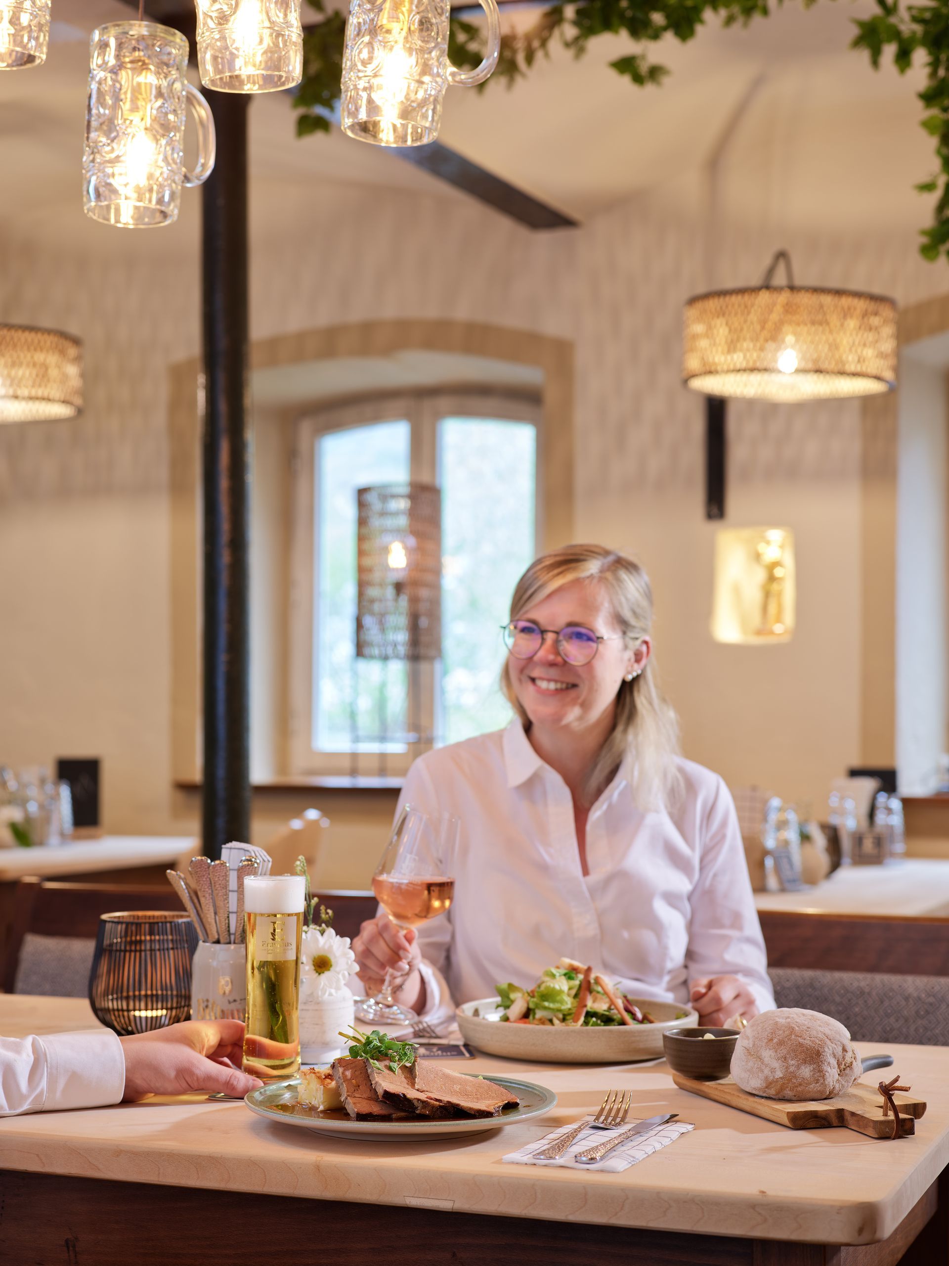 Lächelnde Frau beim Essen in einem Restaurant. Helle Wände, Essen und Getränke auf dem Tisch, rustikale Beleuchtung.