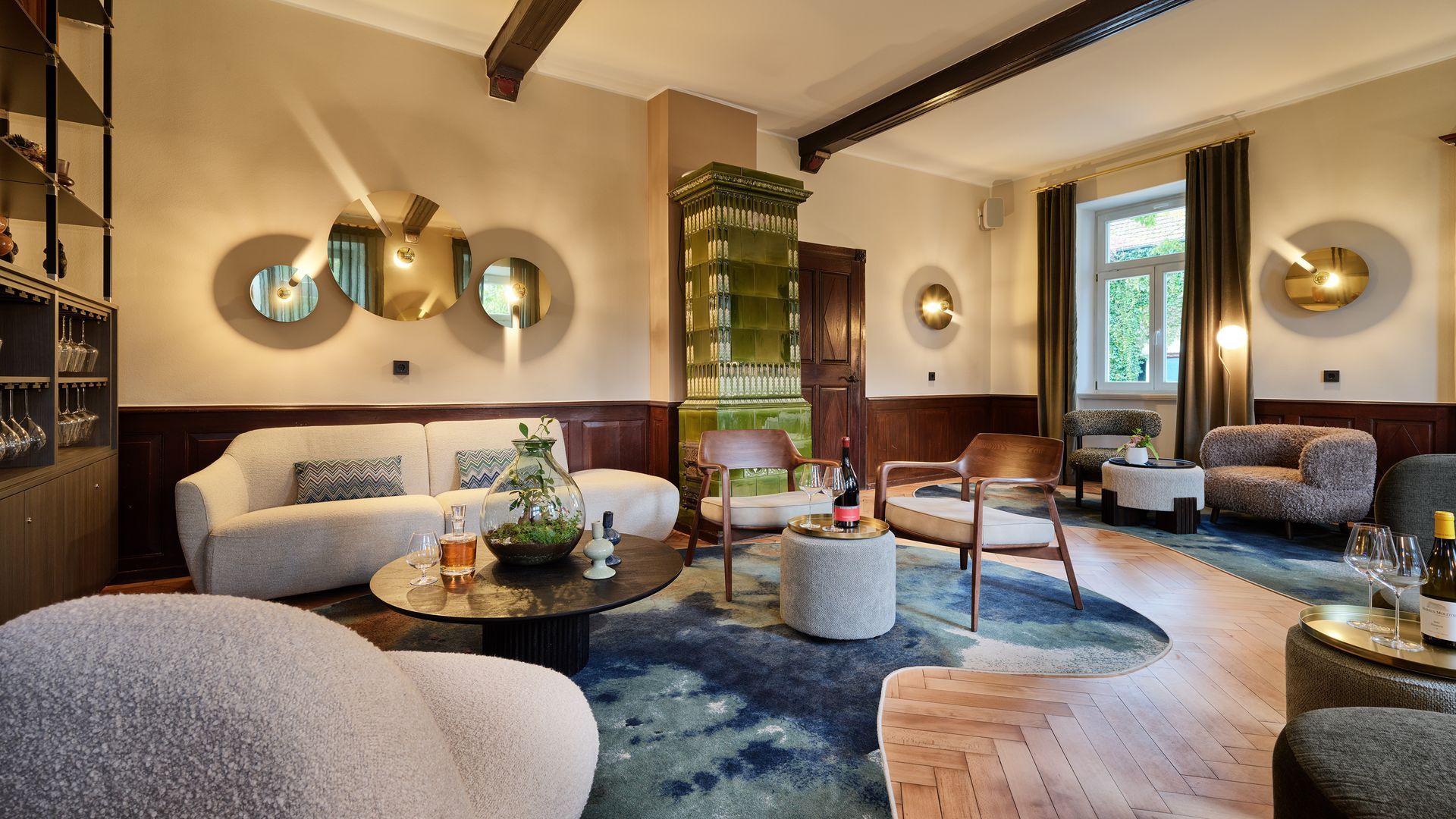 Gemütliches Wohnzimmer mit beigem Sofa, Stühlen, Teppich und kunstvollem Kamin, warme Beleuchtung.