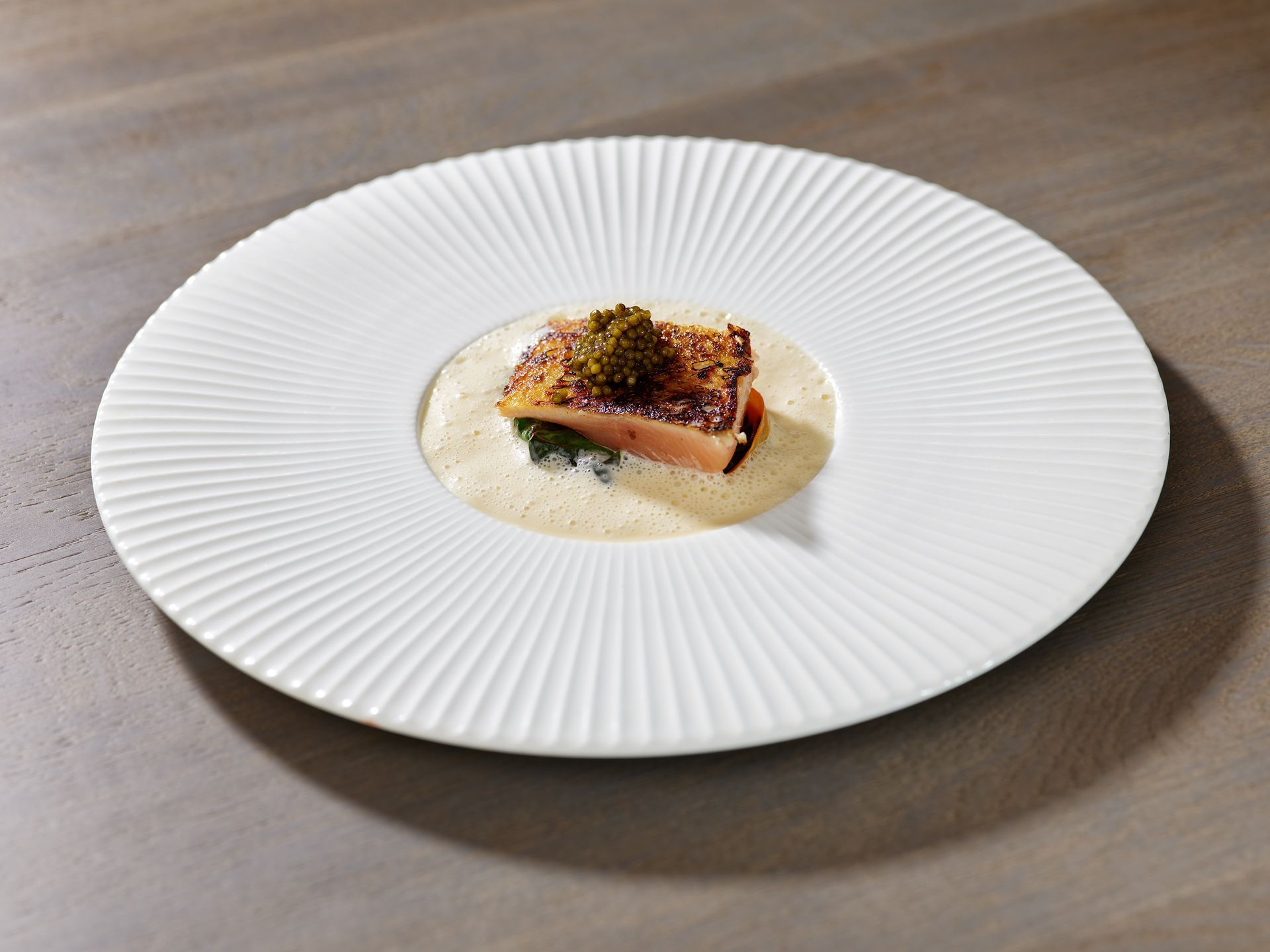 Teller mit gebratenem Fisch mit Sauce und Garnitur. Auf einem weißen Teller.