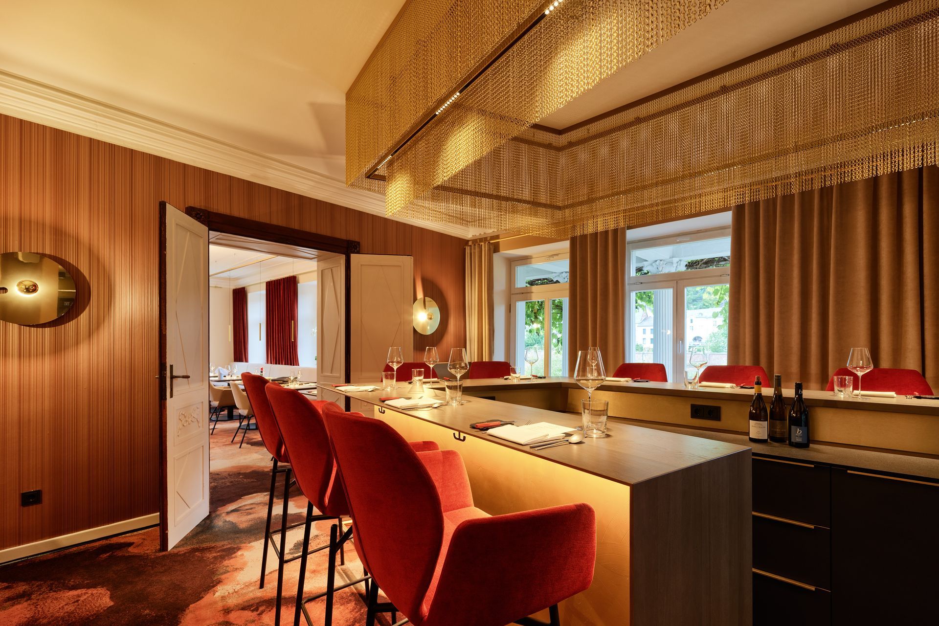 Eine stilvolle Bar mit roten Stühlen, braunen Wänden und einem goldenen Kronleuchter.