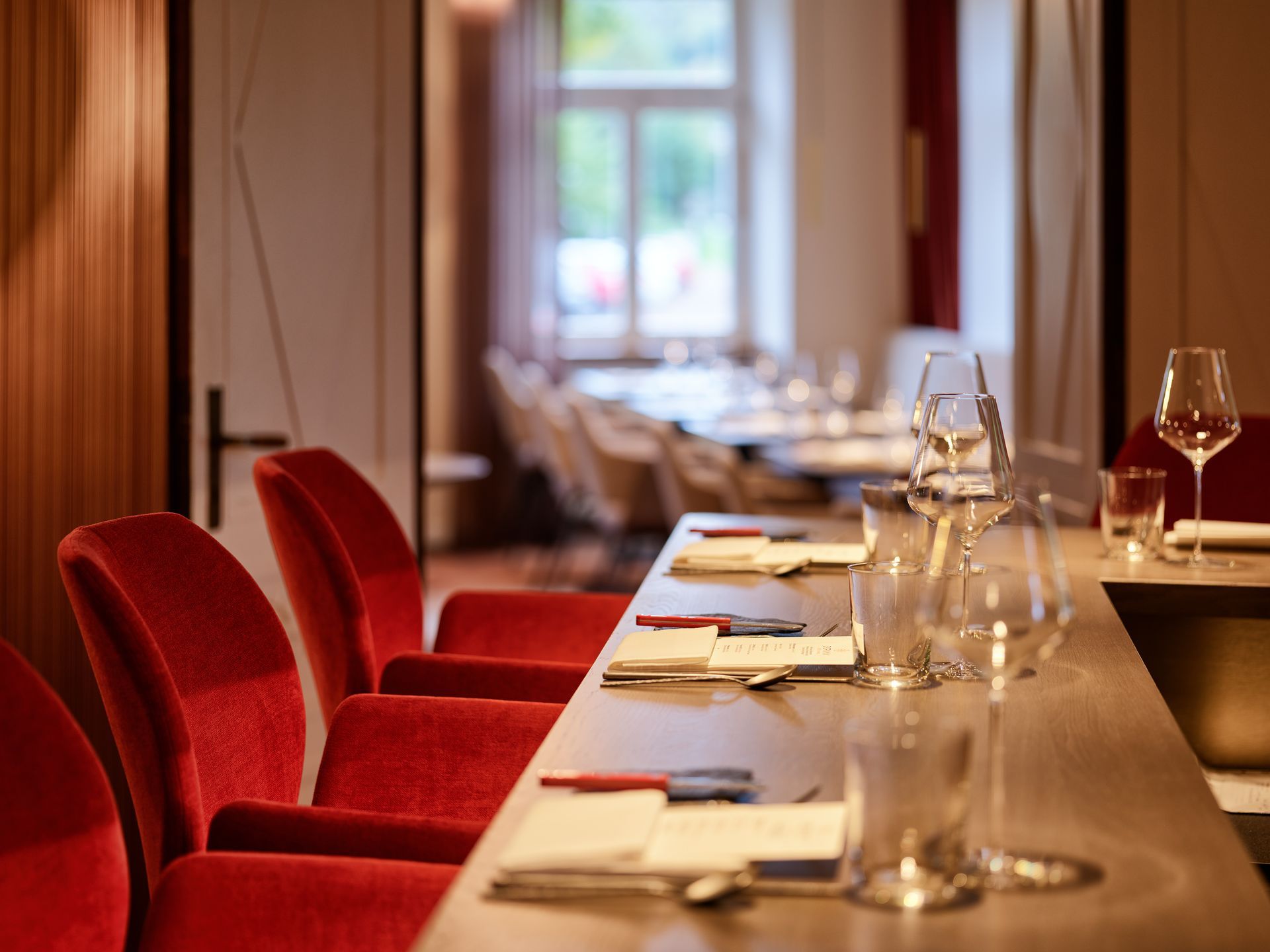 In einem Esszimmer stehen rote Stühle an einem mit Gläsern und Gedecken gedeckten Tisch.