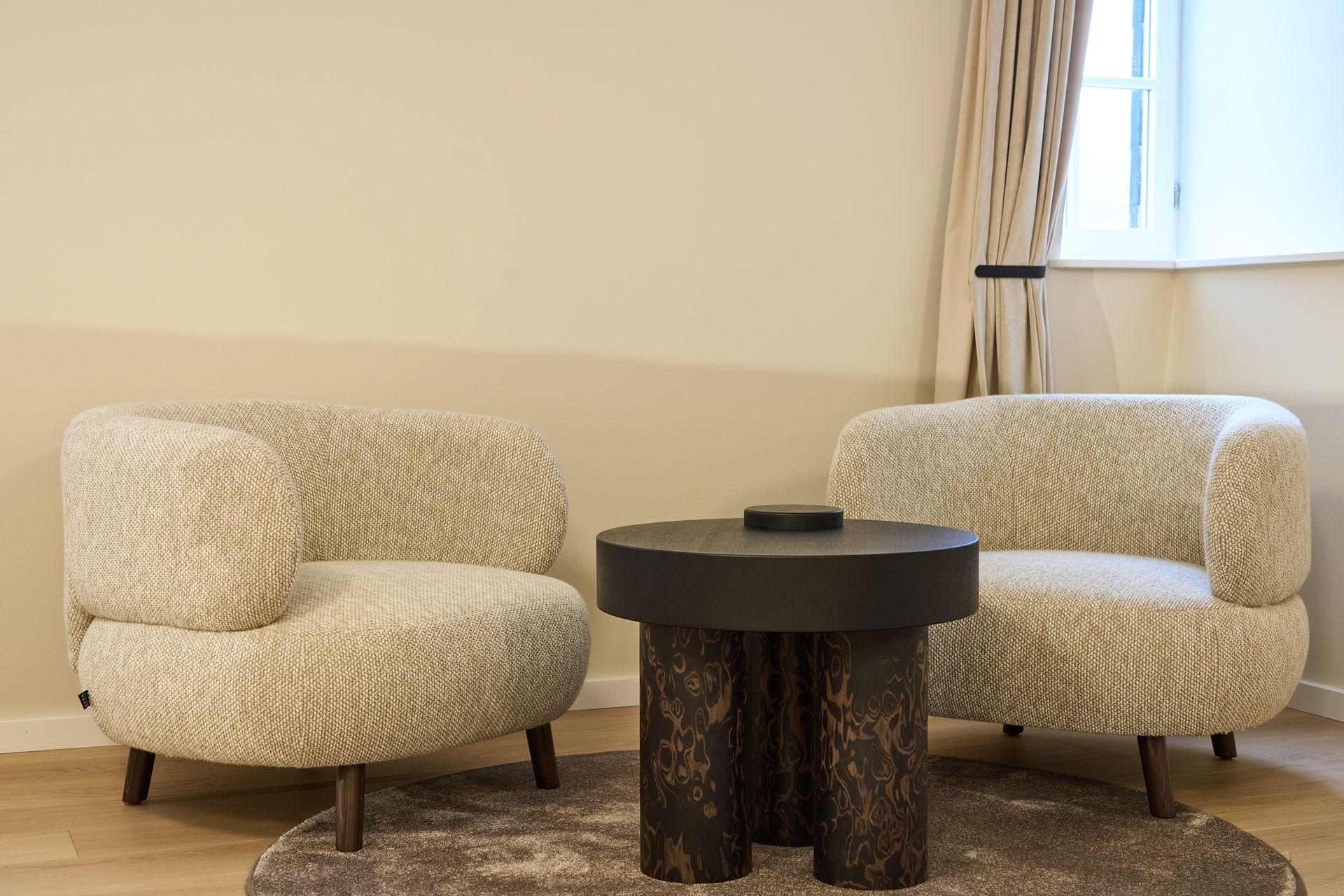 Zwei gemusterte Sessel und ein dunkler Beistelltisch aus Holz auf einem Teppich.