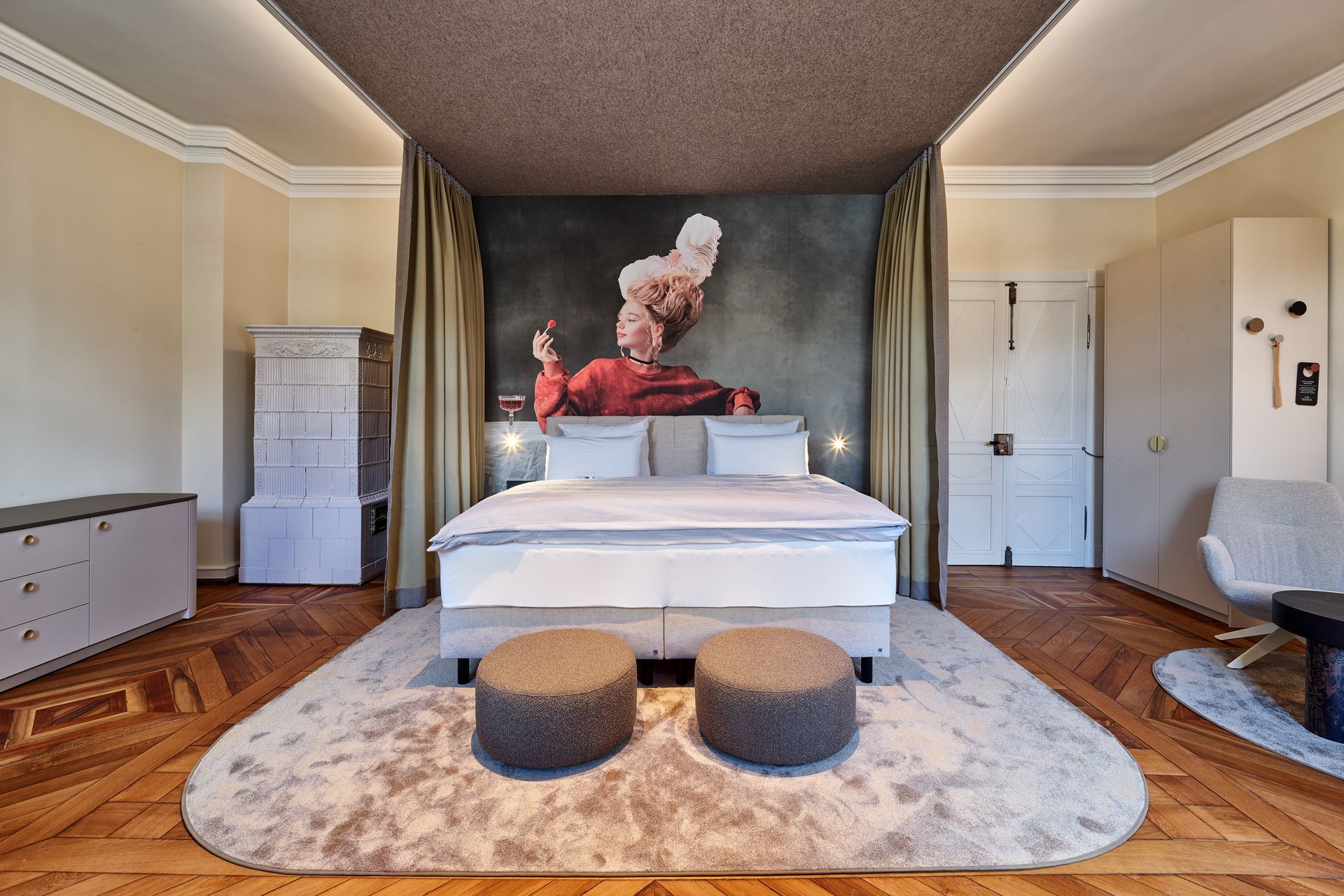 Schlafzimmer mit Bett, Kunstwerken und Sitzgelegenheiten auf einem gemusterten Teppich; heller Holzboden.