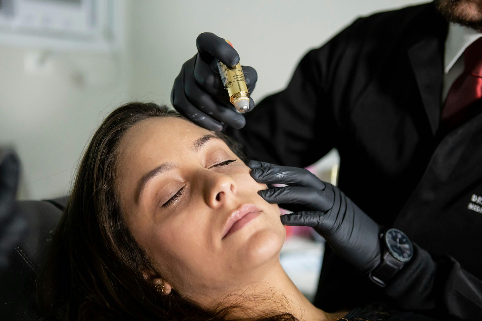 Cosmetic treatment being applied to a woman’s face with gloved hands in a clinic