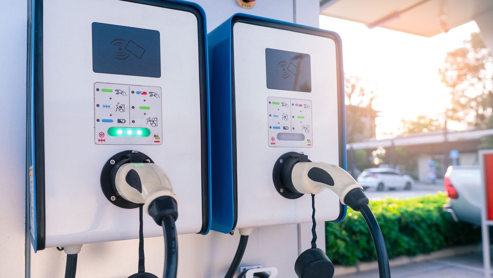 Electric vehicle charging stations, white with blue trim, outdoors, sunlight.