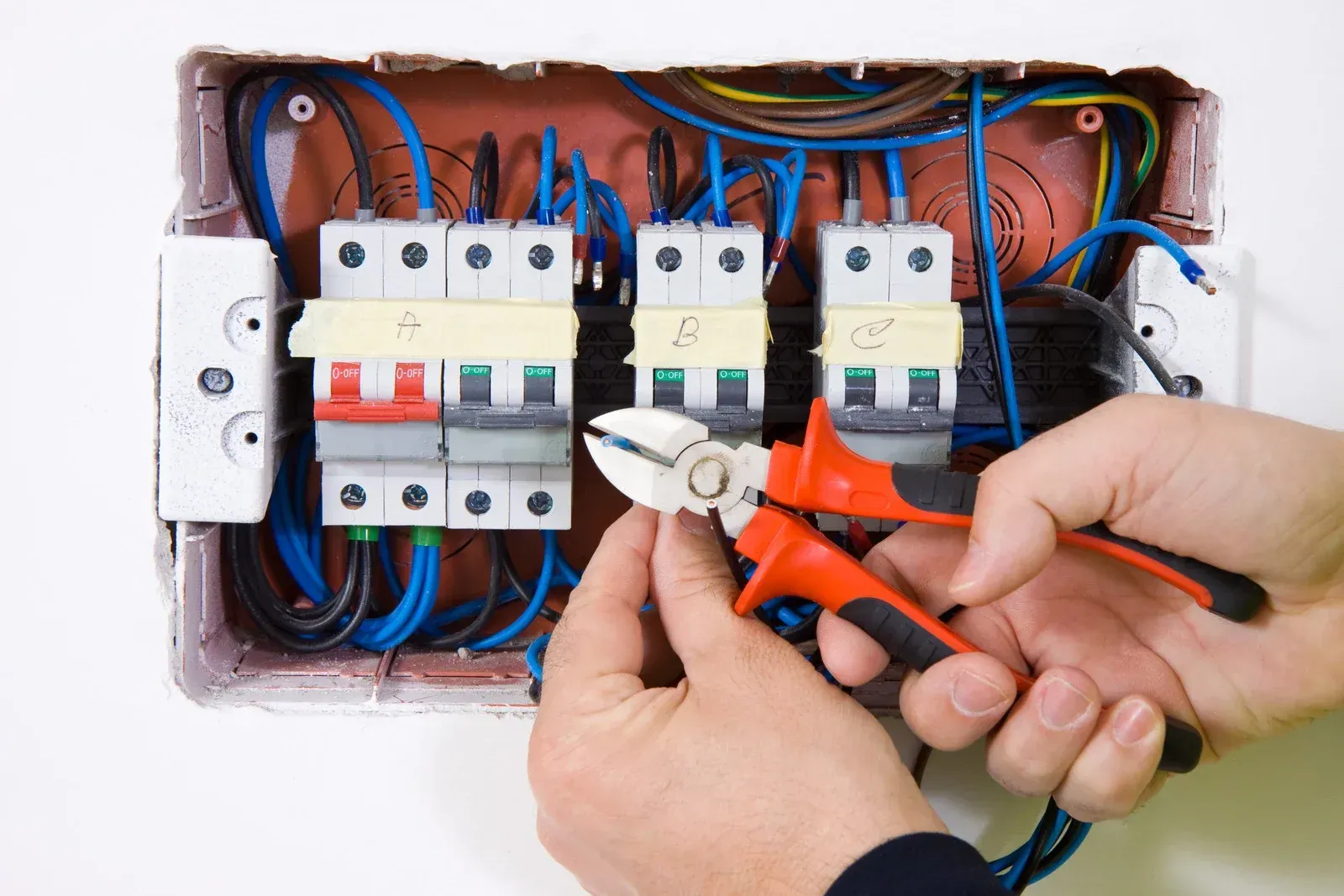 Electrician working on a fuse box, using pliers to cut a wire.