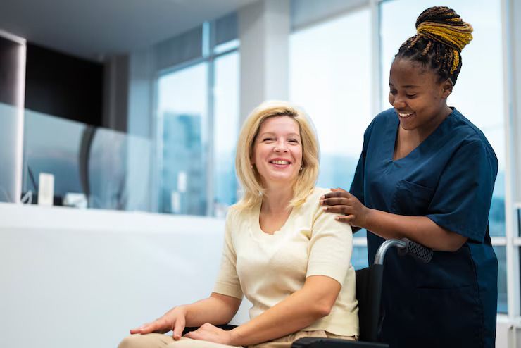 An elderly couple in a wheelchair are sitting on a bench in a park with a nurse.