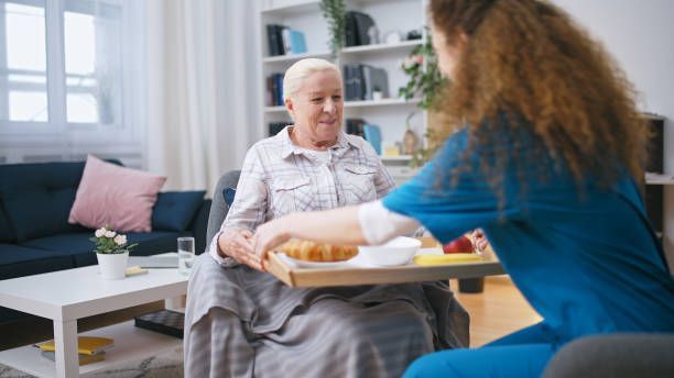 A nurse is serving food to an elderly woman in a living room.