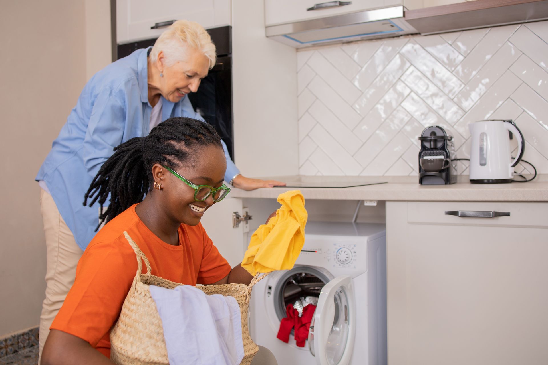 Two women are doing laundry together in a kitchen.
