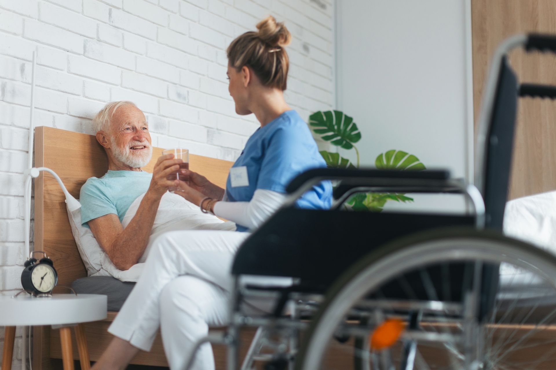 A nurse is holding the hand of an elderly man in a wheelchair.