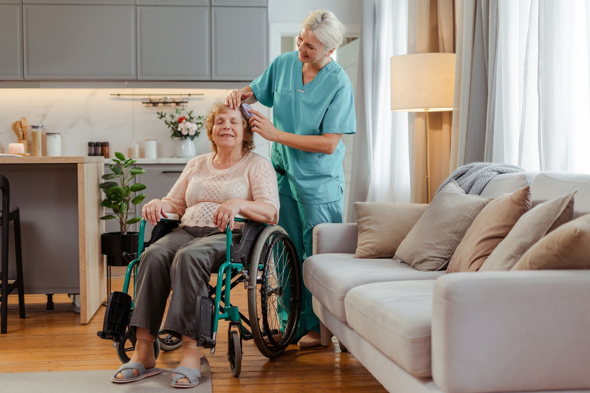 An elderly woman in a wheelchair is being helped by a nurse in a living room.