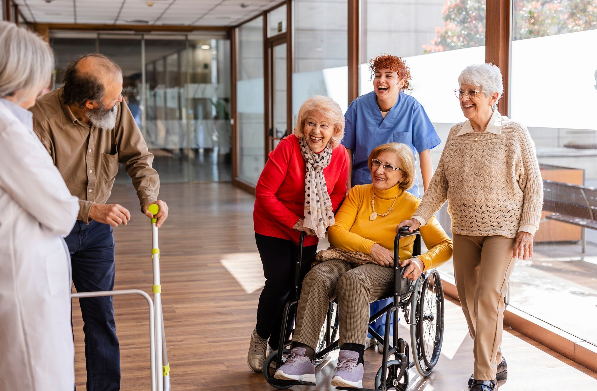 A group of elderly people are standing around a woman in a wheelchair.