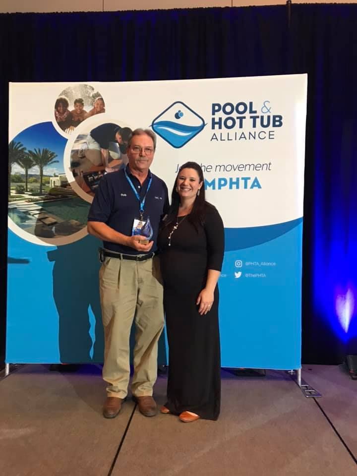 Man holding award with woman in front of a Pool & Hot Tub Alliance banner.