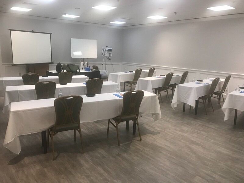 Empty conference room with rows of tables covered in white tablecloths and chairs.