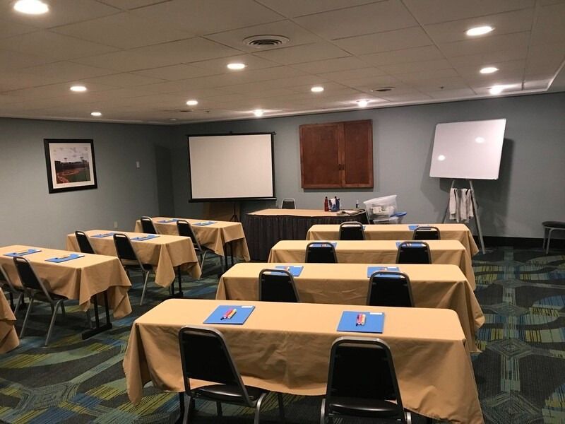 Conference room with tables, chairs, projector screen, and whiteboard.