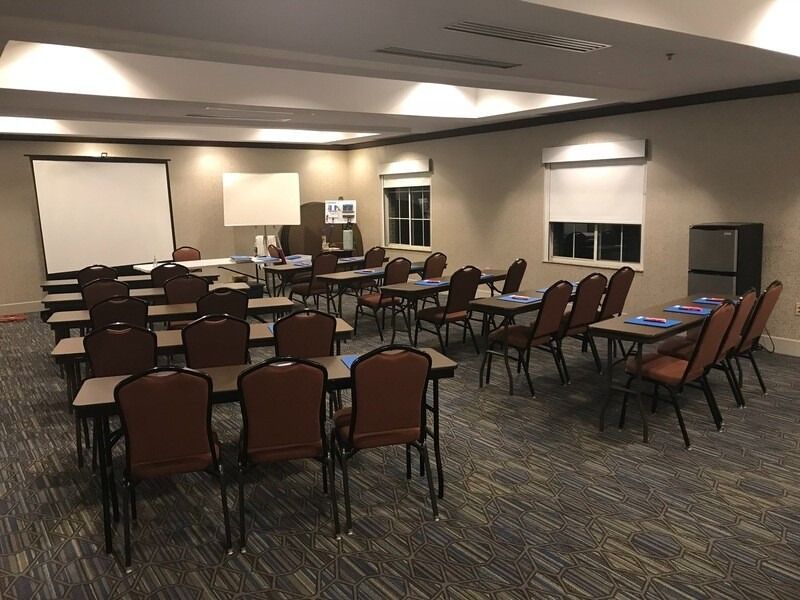 Classroom with rows of tables and chairs, a projector screen, and a water cooler.