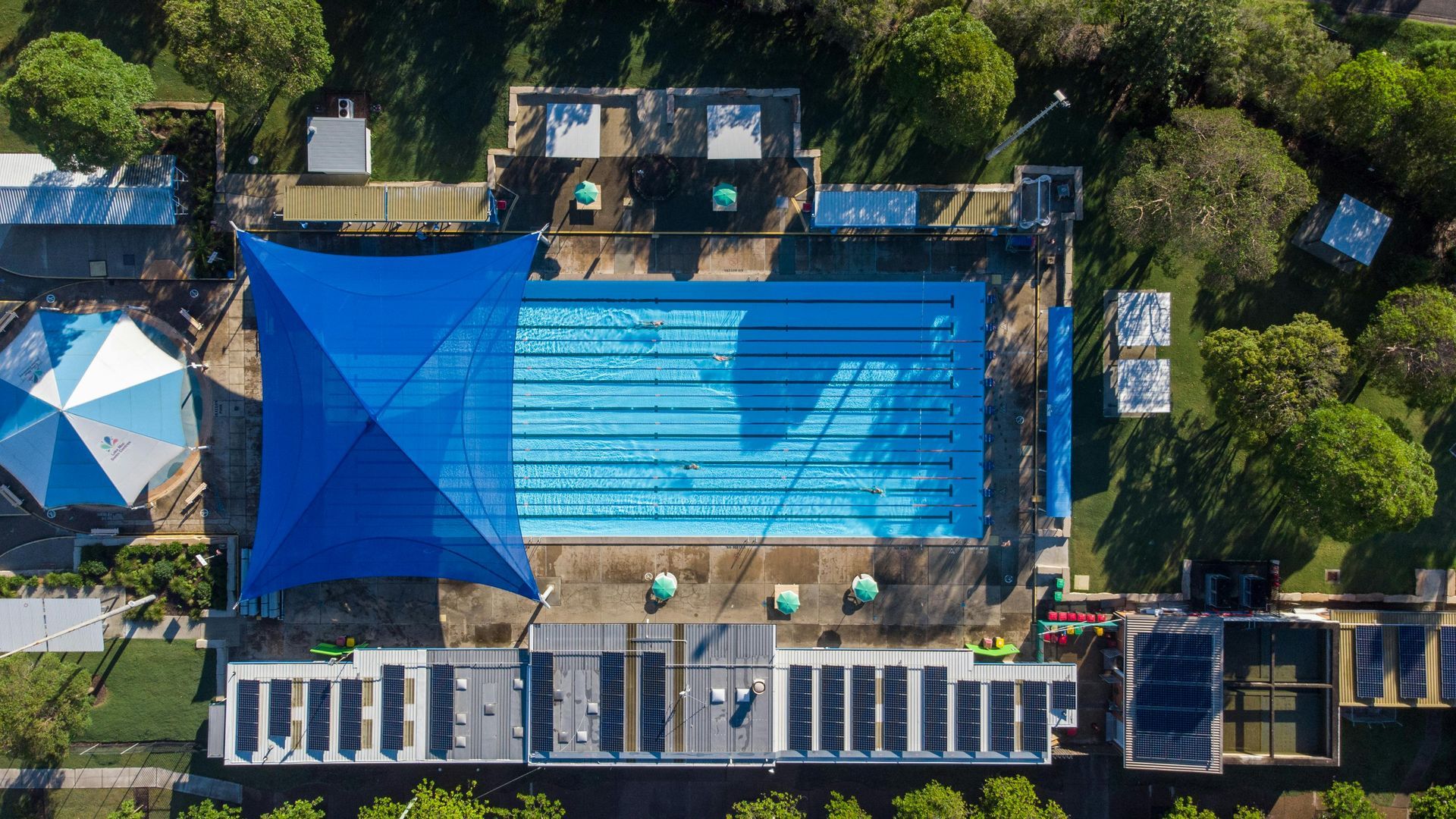 Aerial view of a rectangular swimming pool with lane markers, shaded by a large blue canopy.