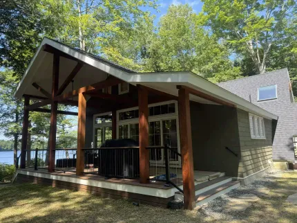 A small house with a porch overlooking a lake surrounded by trees.