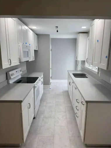A kitchen with white cabinets , a stove , a microwave , and a sink.