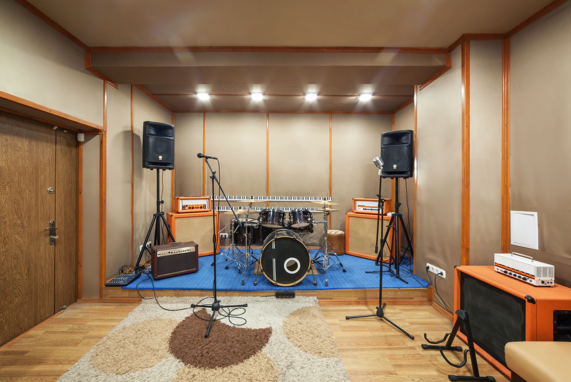 Music recording studio with drum set, speakers, and keyboard. Brown, orange, and blue colors.